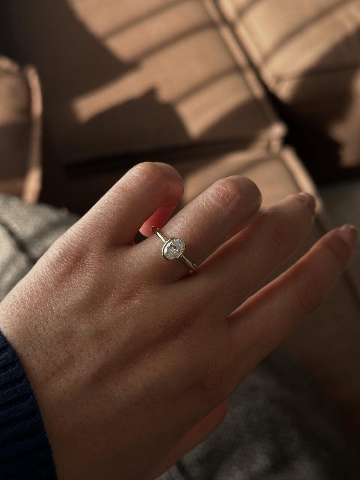 Oval-cut diamond engagement ring on a gold band worn on a finger.