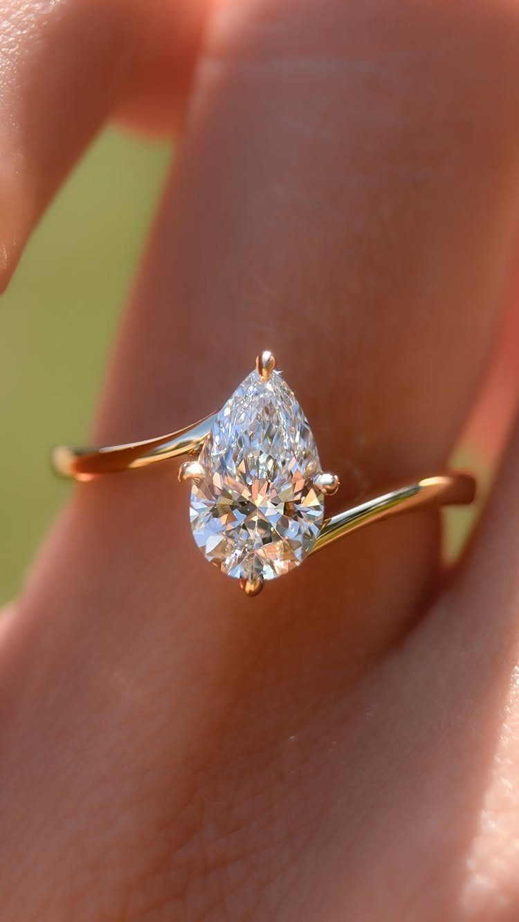 Pear-shaped diamond engagement ring with a gold band on a person's finger.