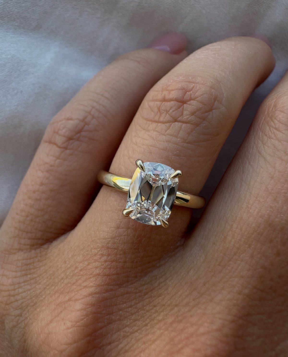 Gold engagement ring with a radiant-cut diamond worn on a person's finger