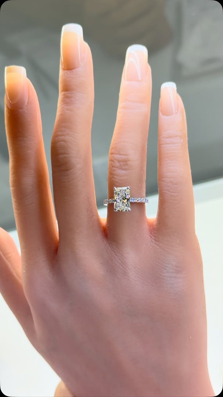 Rectangular diamond engagement ring on a finger with French tip manicured nails.