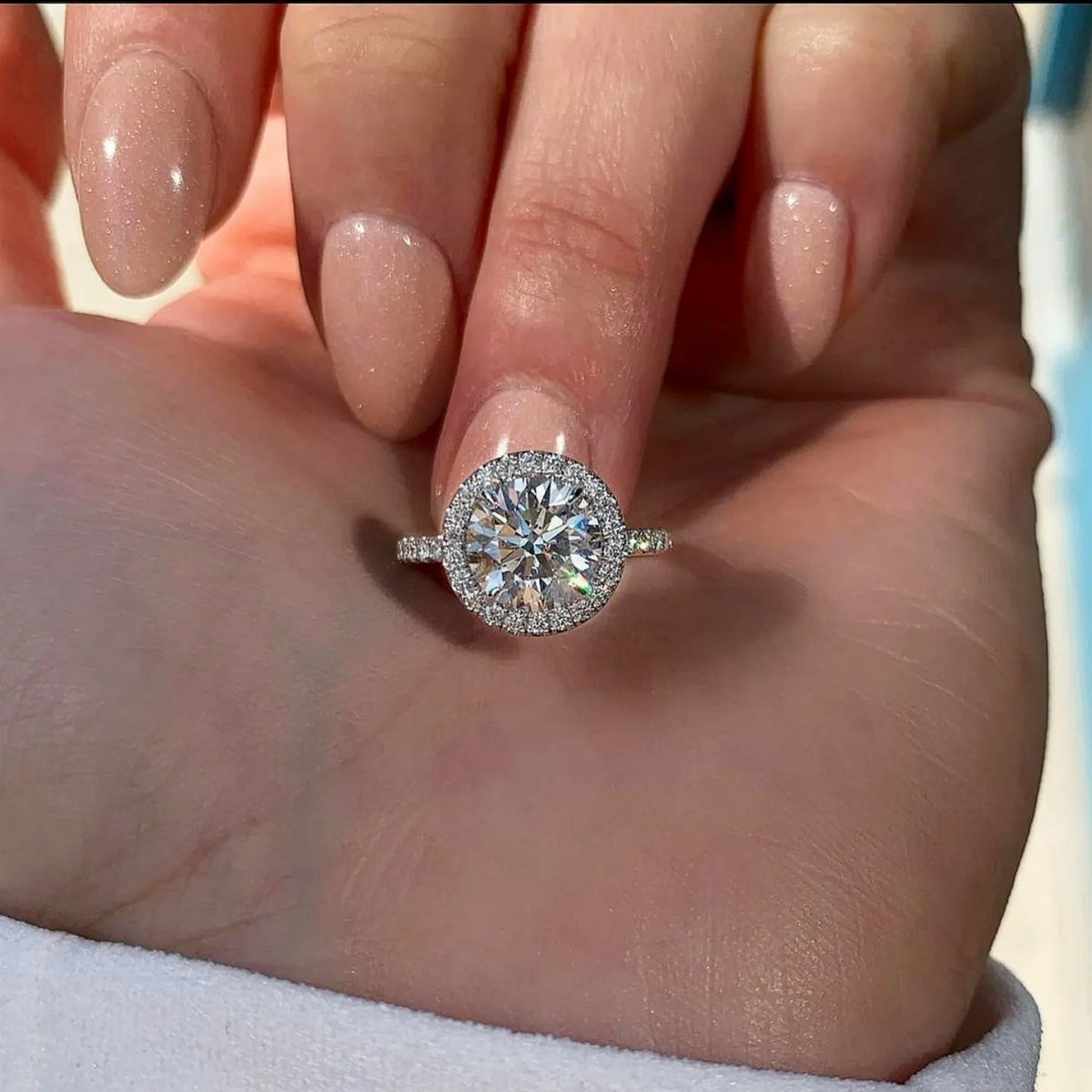 Round diamond engagement ring with a halo setting held in a hand