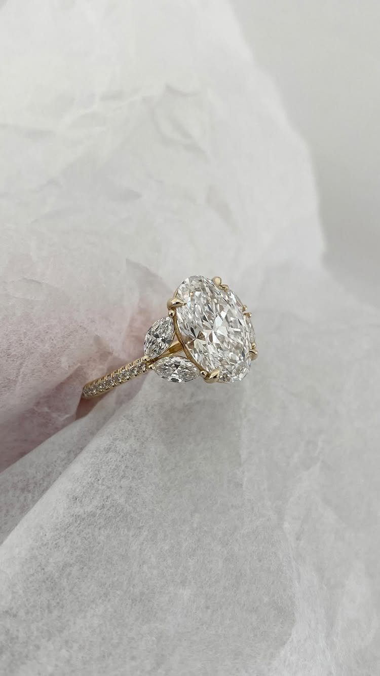 Oval-cut diamond engagement ring with side stones resting on white crystal surface