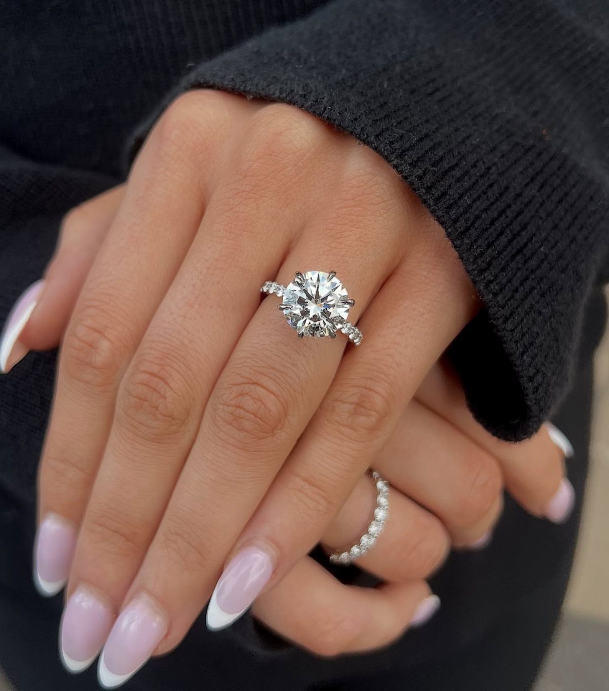 Round diamond engagement ring and wedding band on a hand with French nails