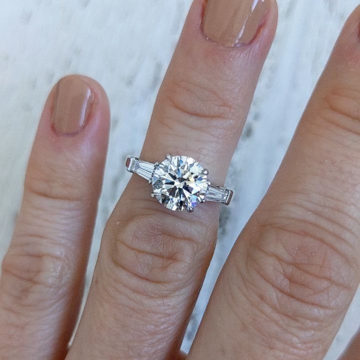 Diamond engagement ring with round center stone and baguette side stones on finger