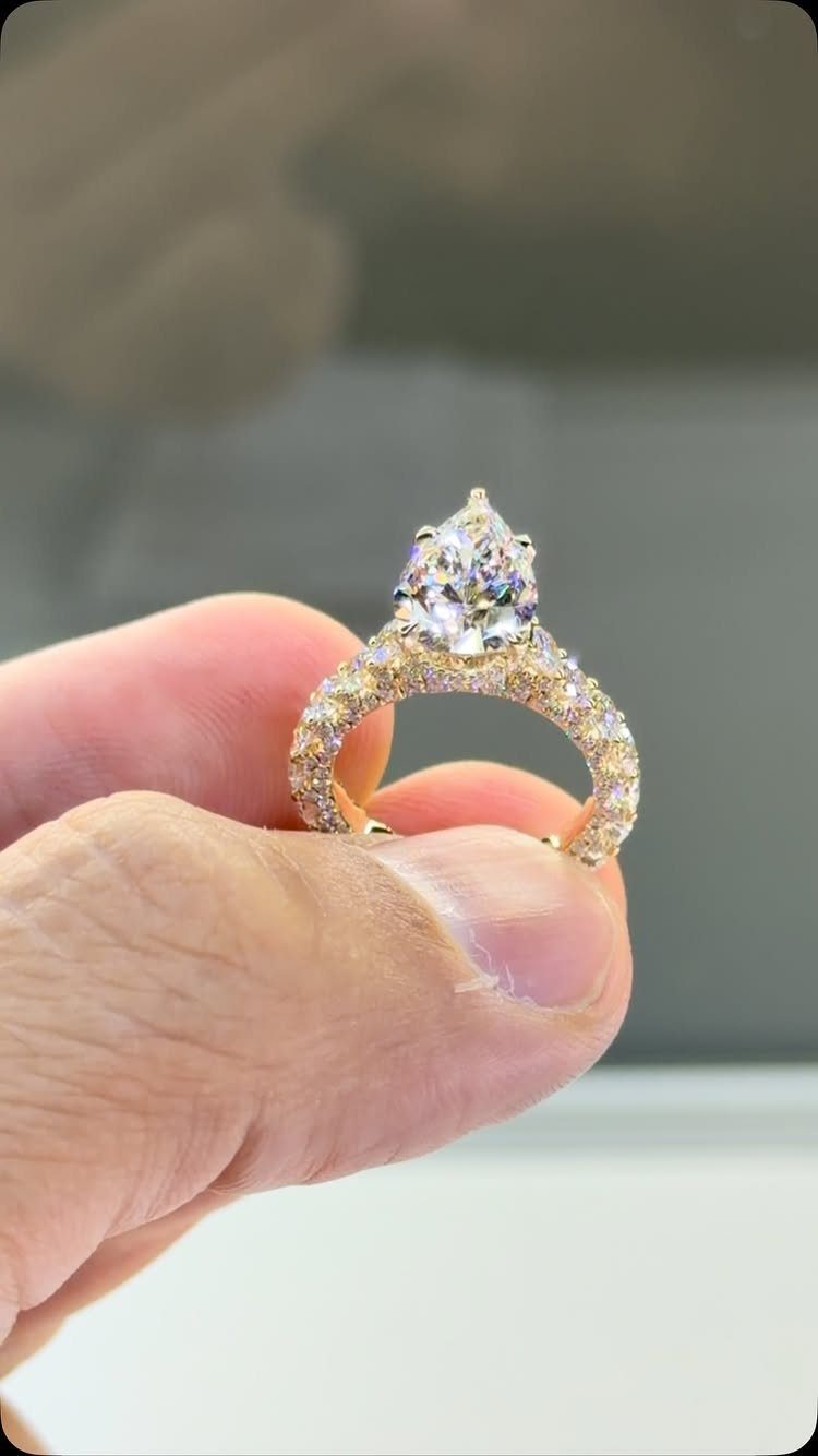 Gold diamond ring with pear-shaped center stone held between two fingers.