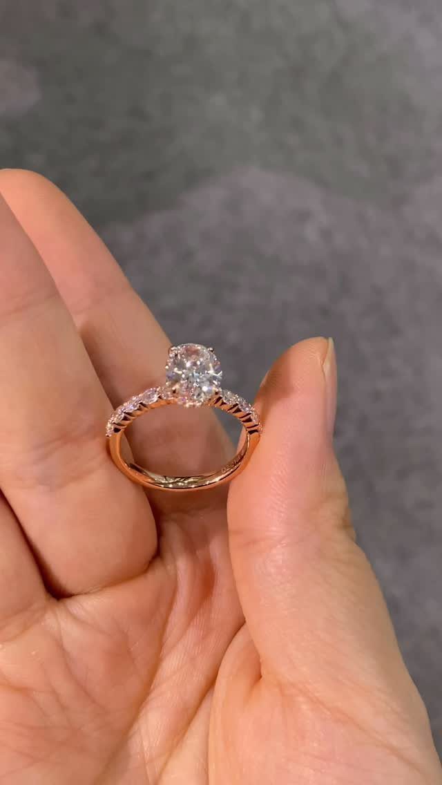 Rose gold diamond engagement ring held between a person's thumb and finger.
