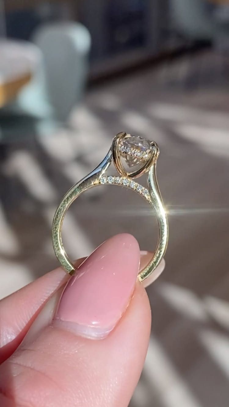 Gold diamond ring with a round cut stone held by a manicured finger.