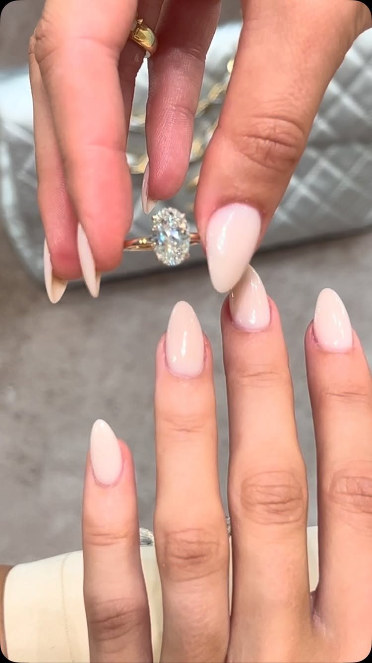 Gold ring with a large oval diamond held by fingers with pink nails.