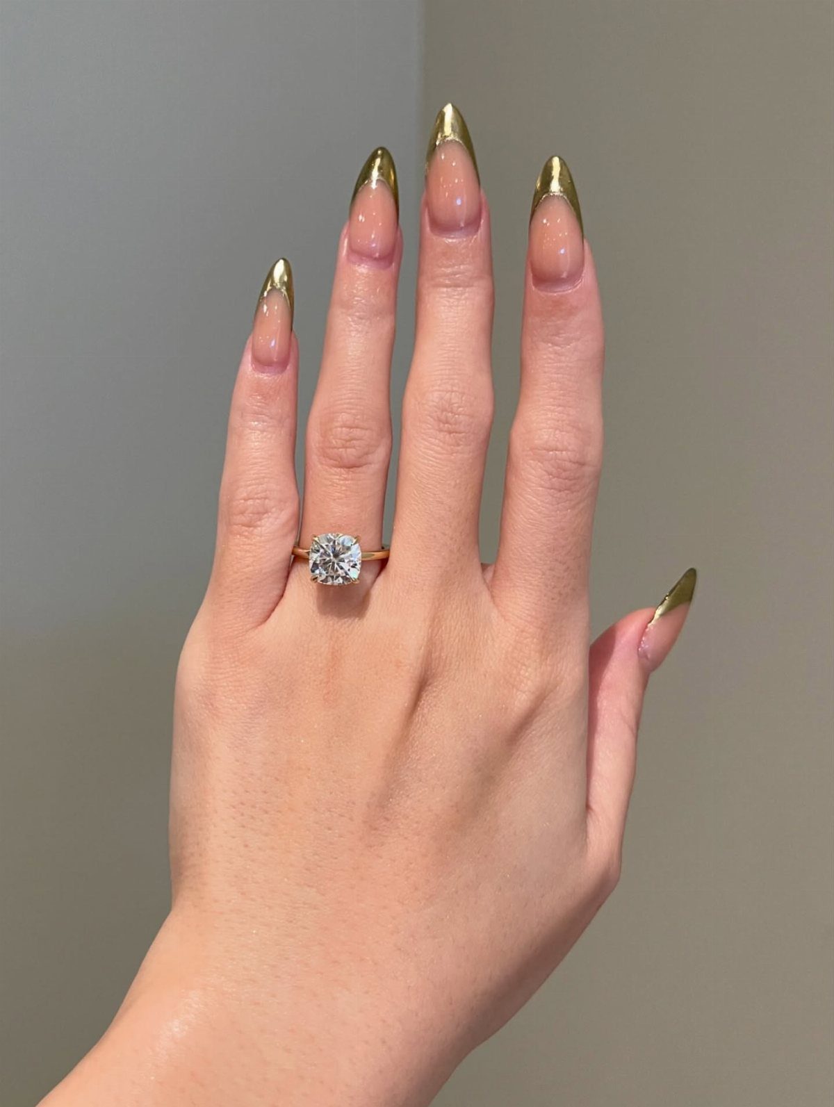 Gold ring with a large square diamond on a hand with gold nails.
