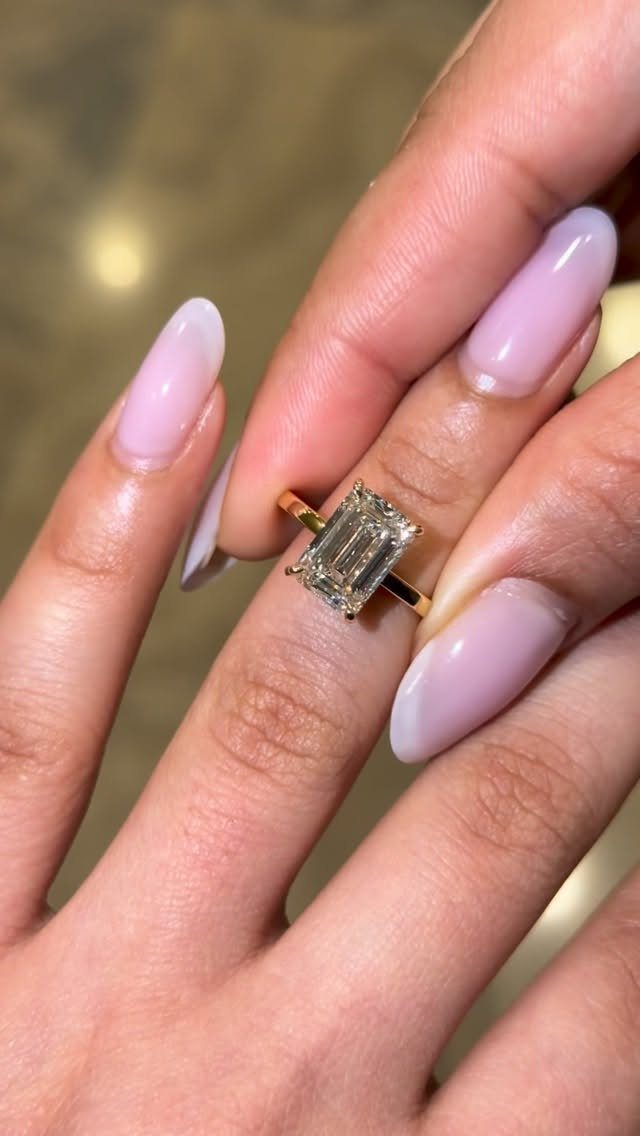 Emerald-cut diamond ring with a yellow gold band on a manicured finger