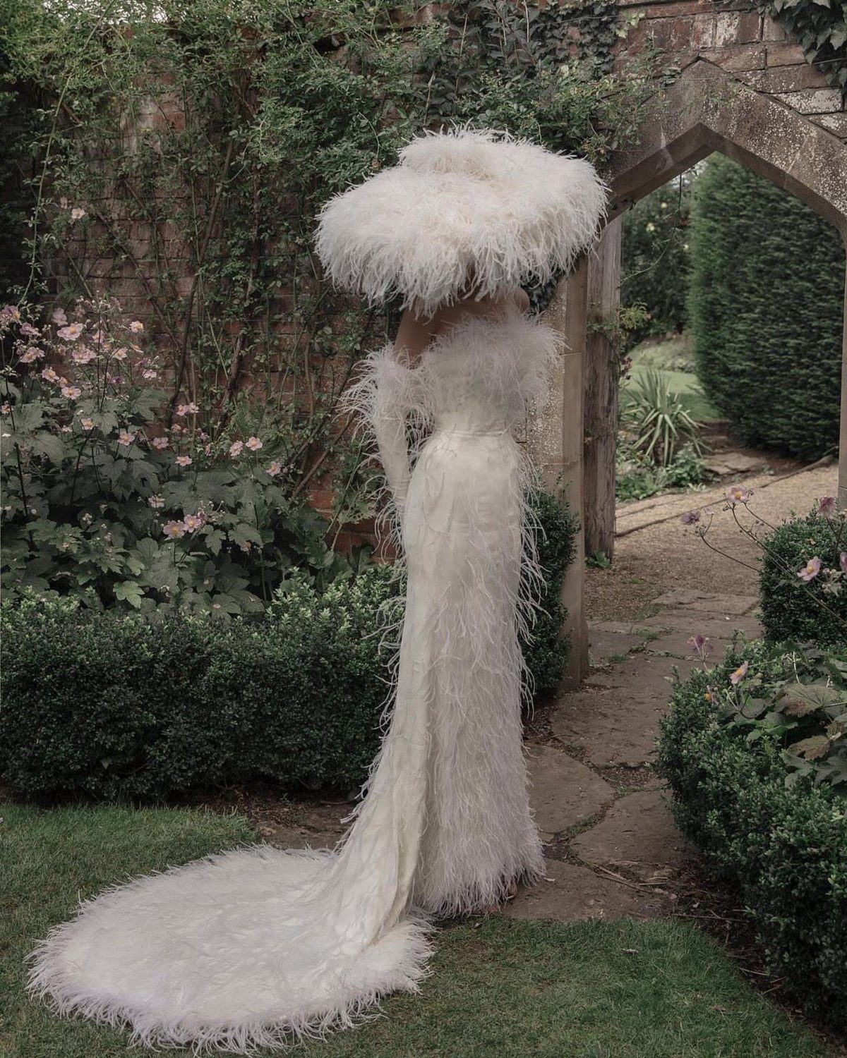 White feather gown and oversized hat worn by a person in a garden.