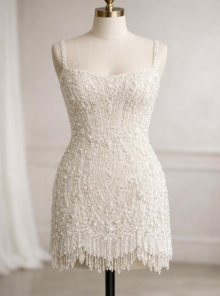 Short white beaded wedding dress with fringe on a mannequin against a wall