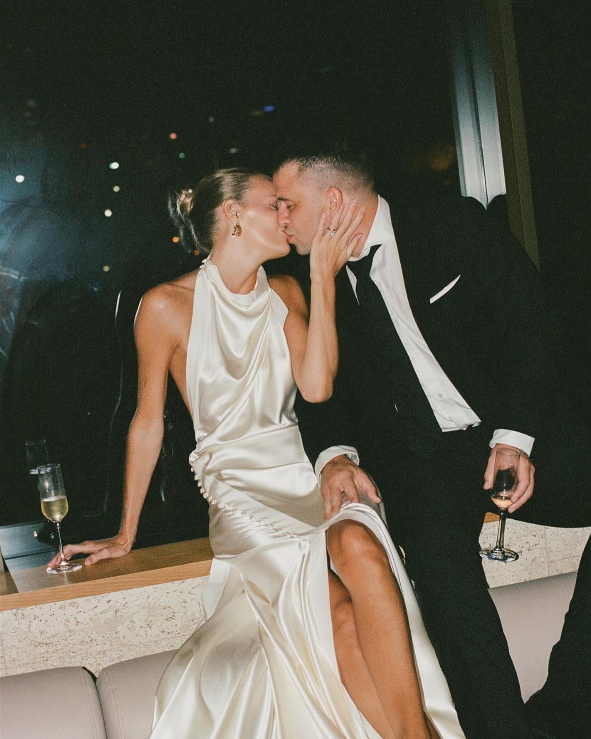 Couple kissing, woman wearing a white satin halter-neck dress with a high slit.