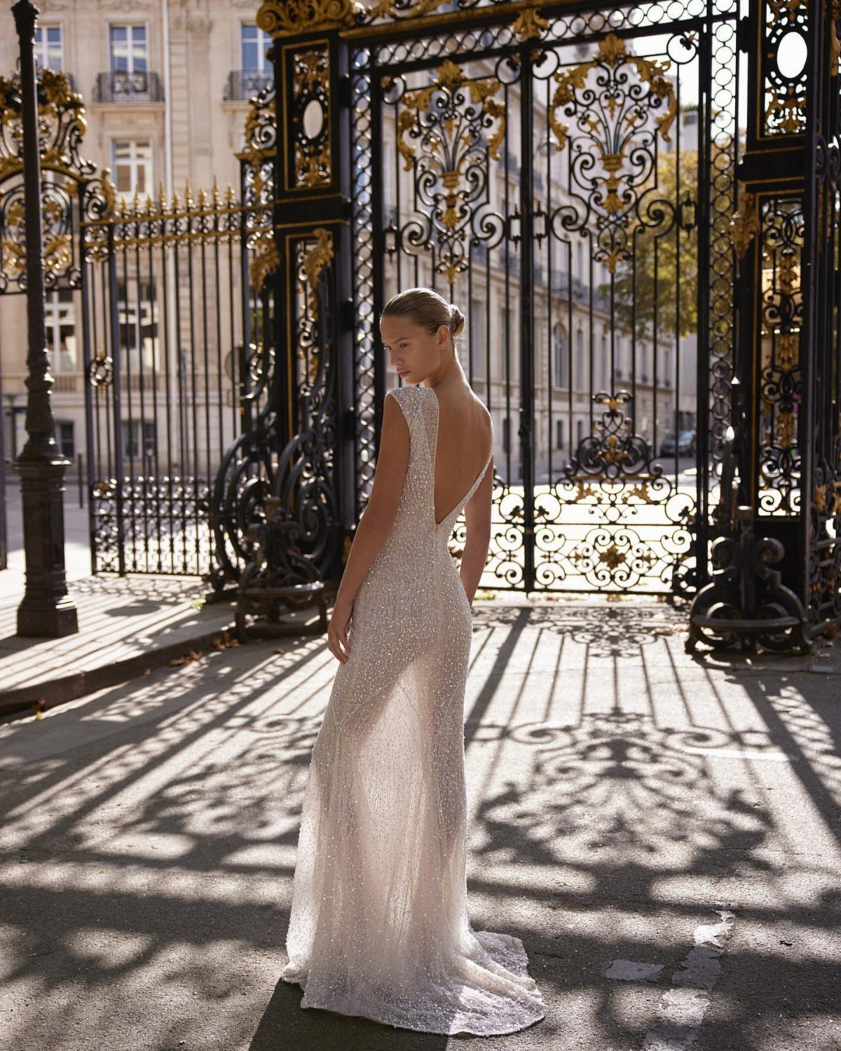 Woman in a white sparkly bridal gown with an open back by ornate gates.