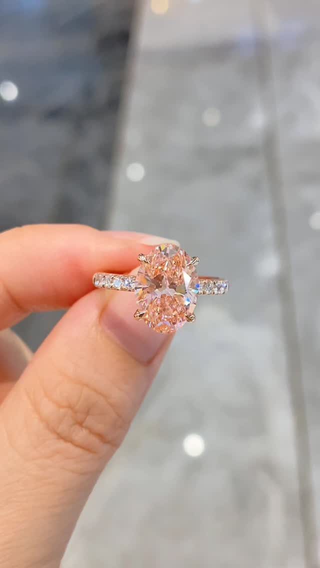 Rose gold engagement ring with a peach almond shaped gemstone held by fingers