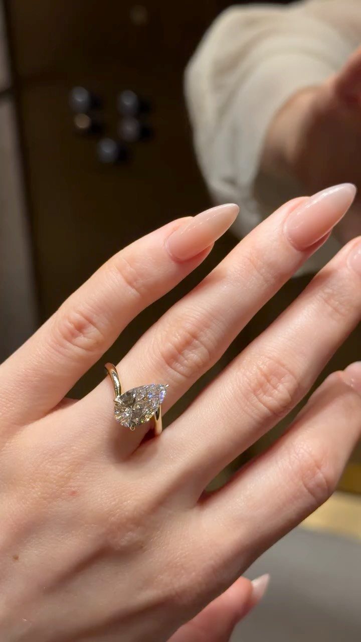 Gold solitaire engagement ring with almond-shaped diamond on a manicured finger