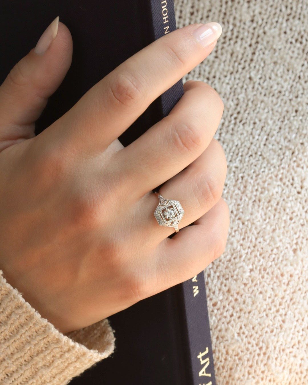 Silver-toned Art Deco engagement ring with geometric halo on a person's finger