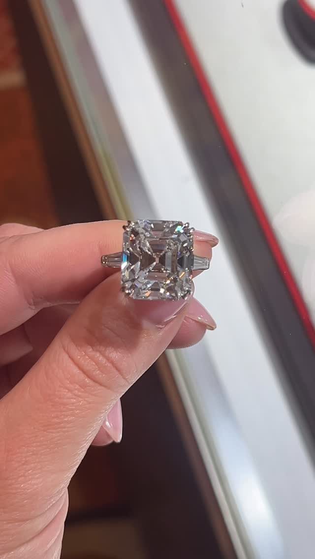 Emerald-cut diamond engagement ring with antique setting held between a person's fingers.