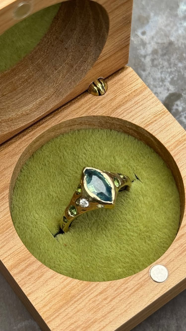 Gold ring with marquise blue gemstone in a wooden box with green velvet.
