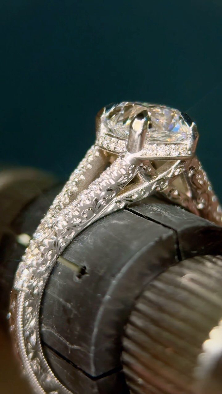 Intricately engraved silver engagement ring with a large diamond held in a clamp.