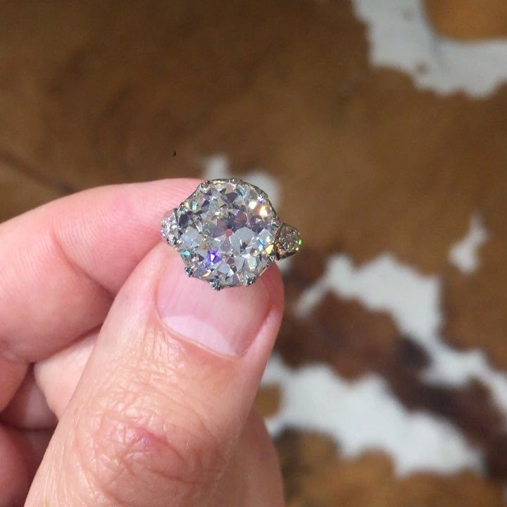 Gold engagement ring with a large oval diamond in an antique setting held by fingers