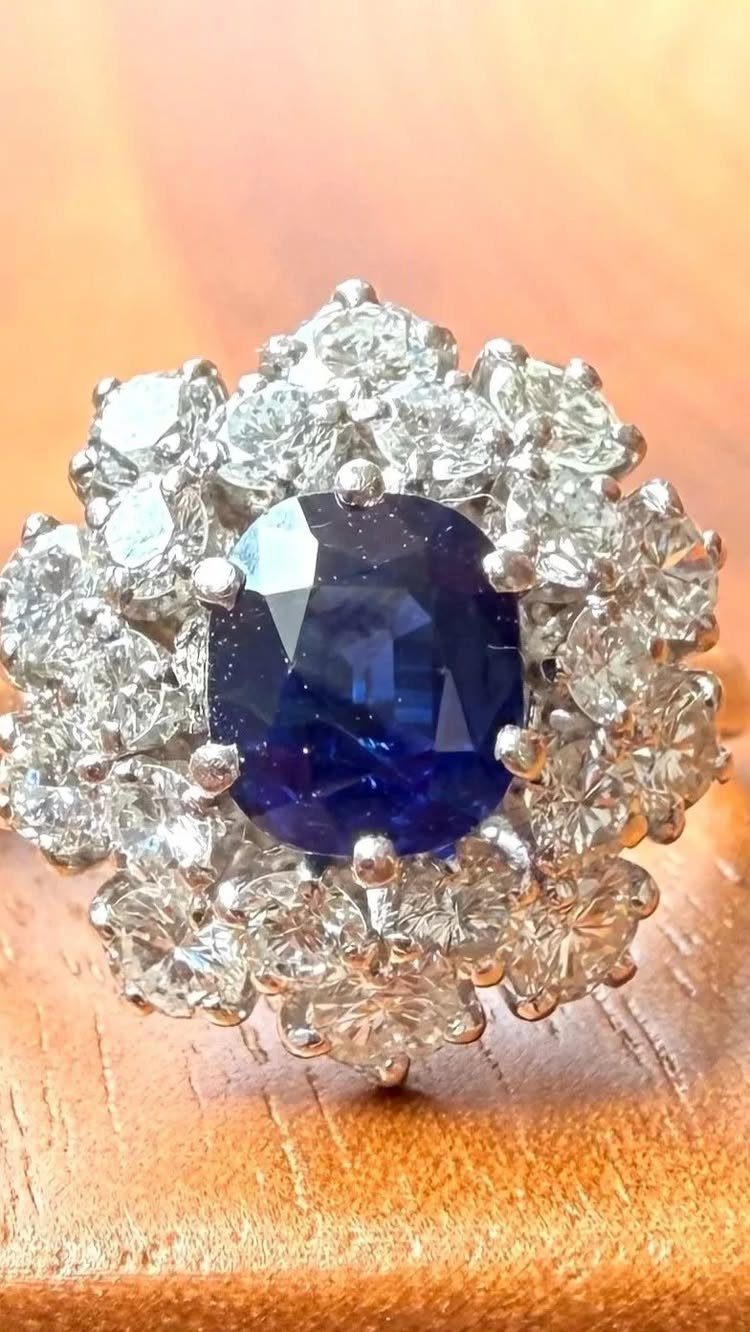 Oval blue sapphire ring surrounded by a cluster of clear diamonds on wood