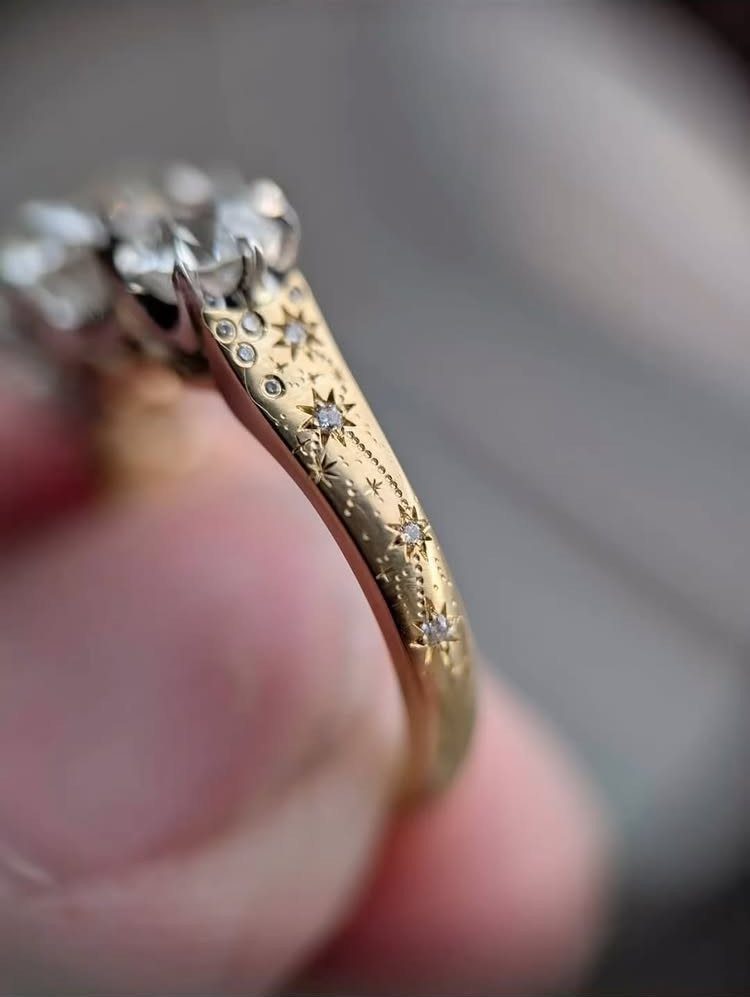Gold engagement ring with star engravings and diamonds held between fingers