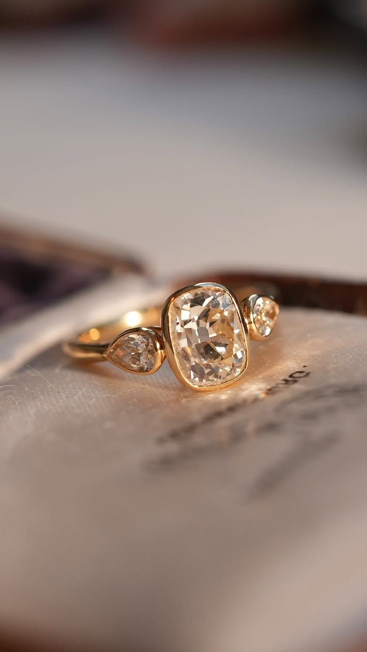 Gold engagement ring with cushion-cut center diamond and pear-shaped side stones.
