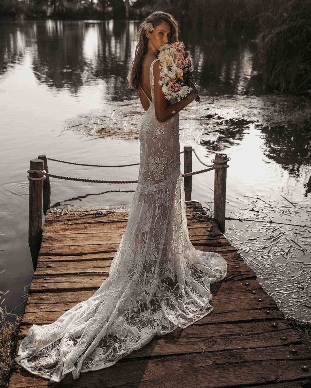 Woman in a white lace wedding dress with a train on a wooden dock