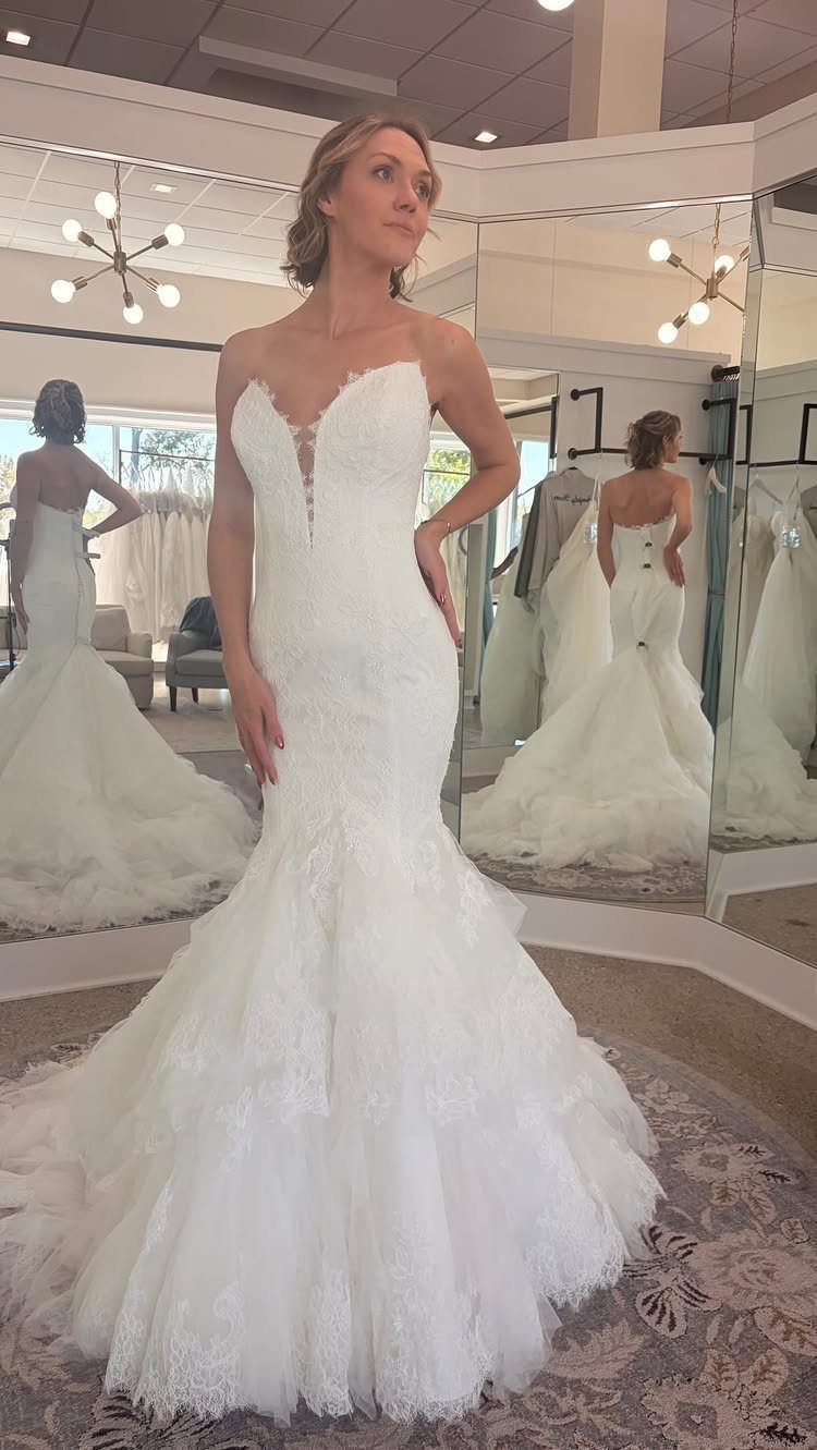 Woman in a white strapless lace mermaid wedding dress posing in a bridal boutique