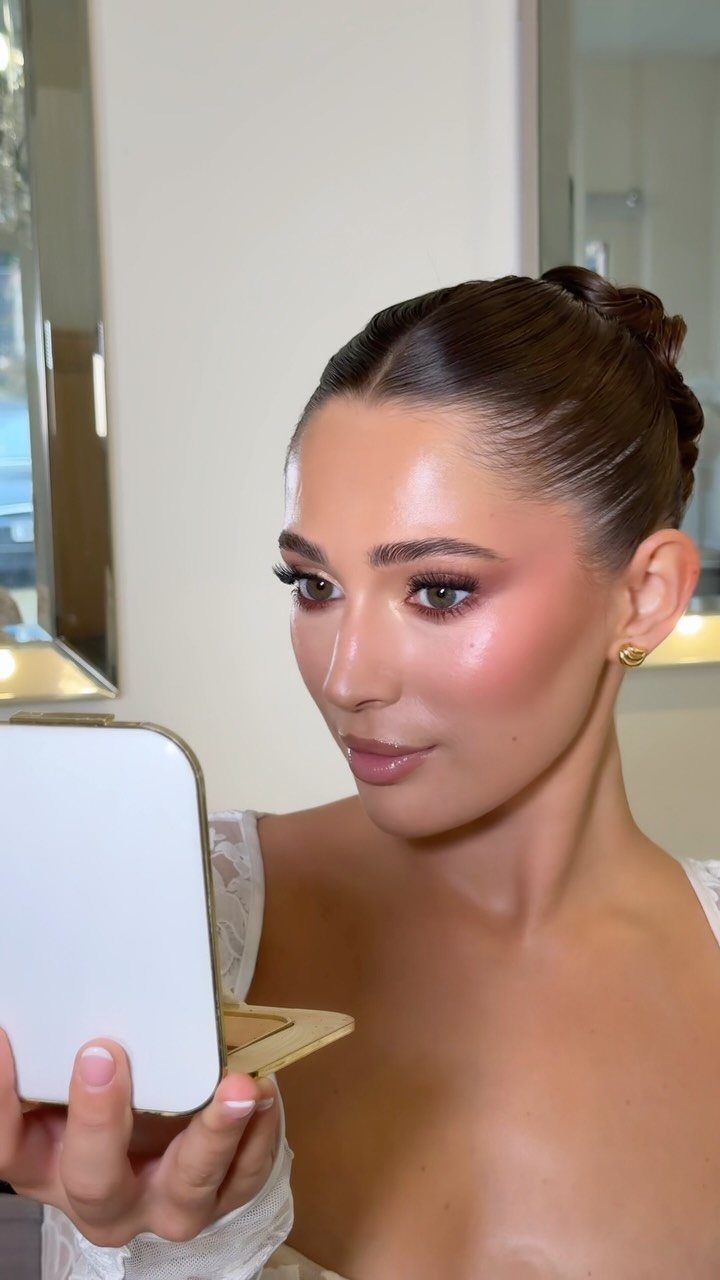 Woman with green eyes and bridal makeup looking into a small handheld mirror