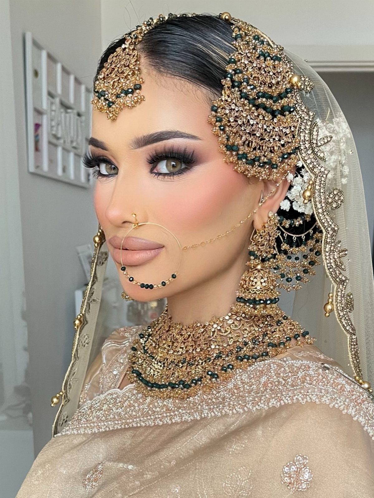 Woman with green eyes wearing gold bridal makeup and traditional Indian jewelry