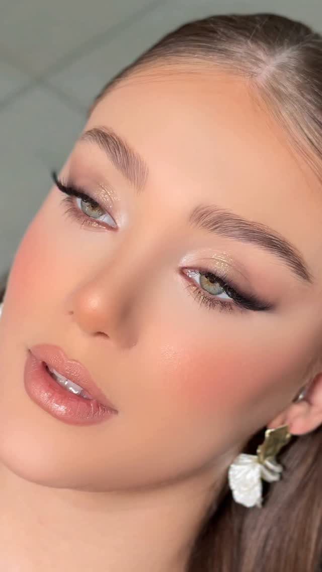 Woman with green eyes wearing gold shimmer eyeshadow and glossy nude lipstick.