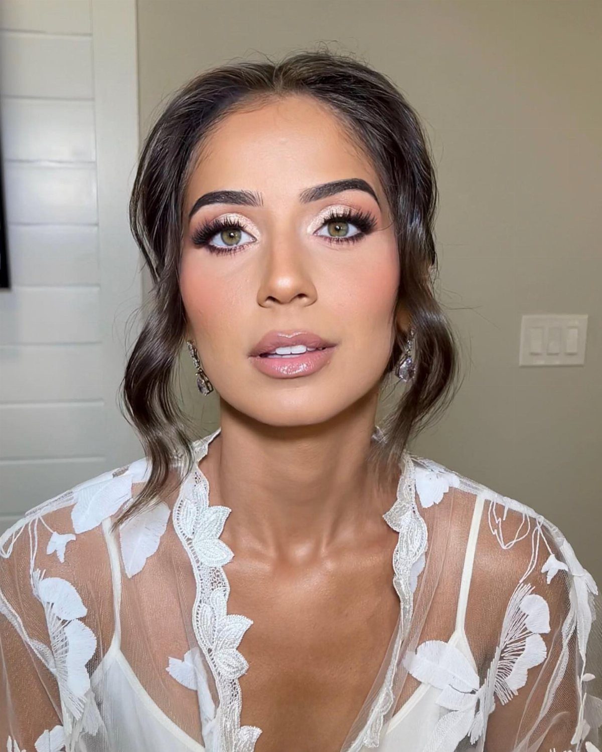Woman with green eyes wearing bridal makeup and a white lace bridal robe.