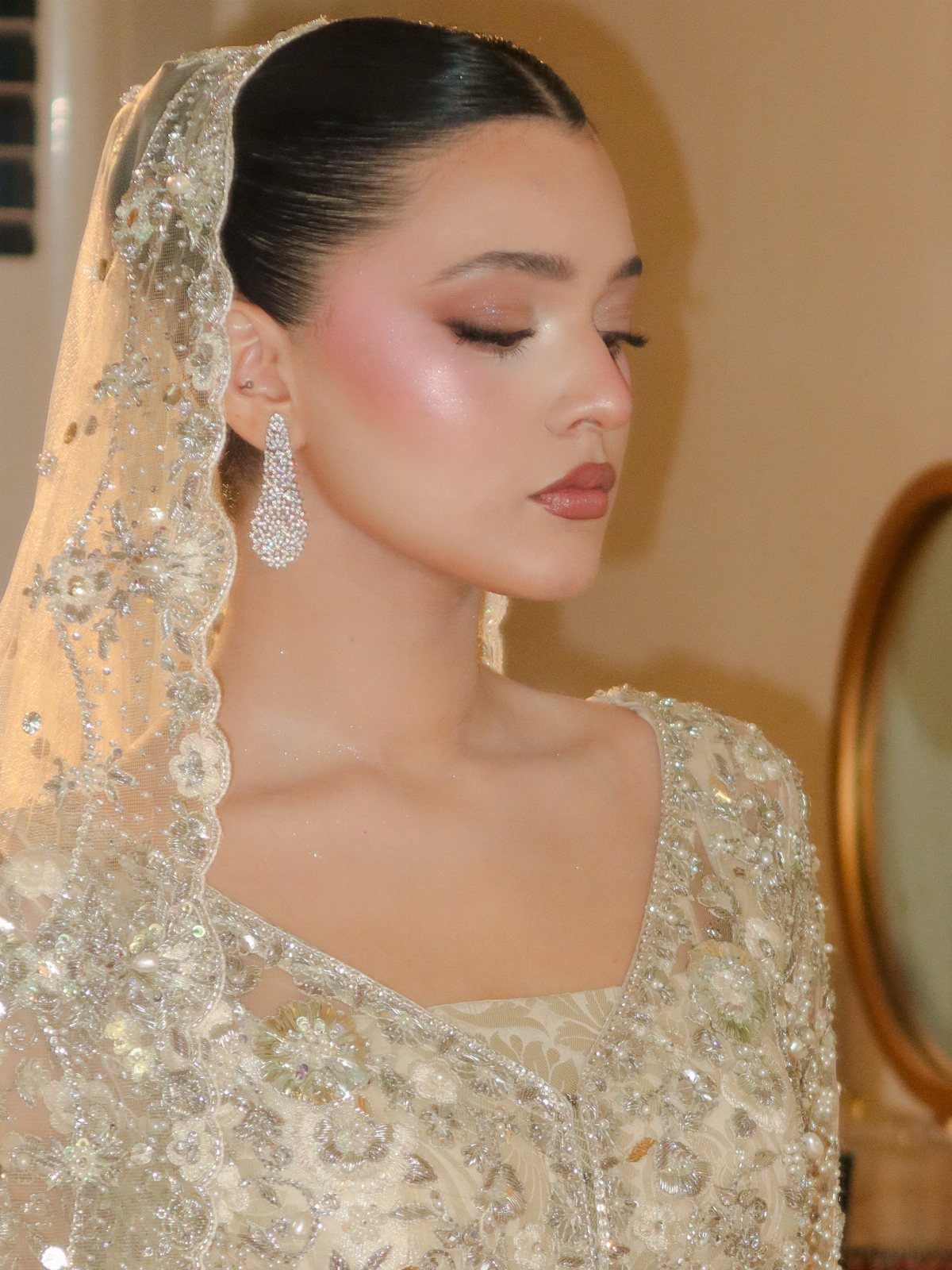 Woman with pale skin wearing bridal makeup and an embellished cream bridal outfit.
