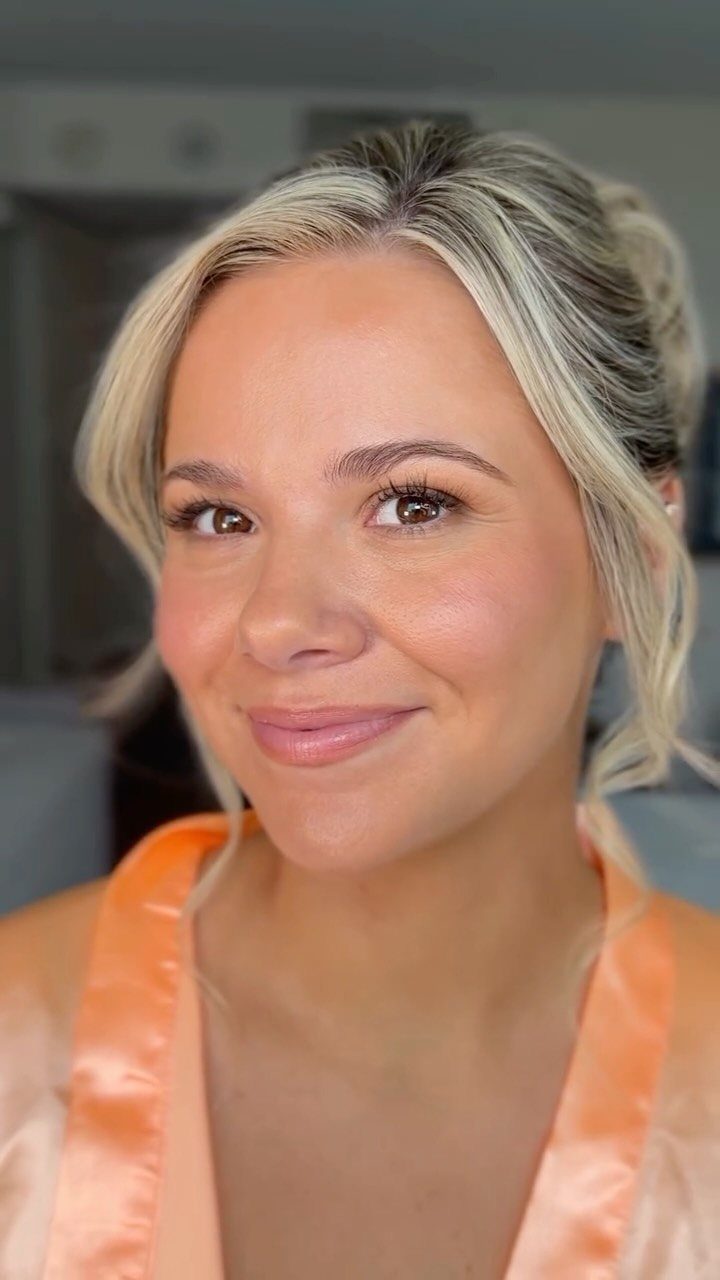 Woman with blonde hair and bridal makeup wearing a peach satin robe.