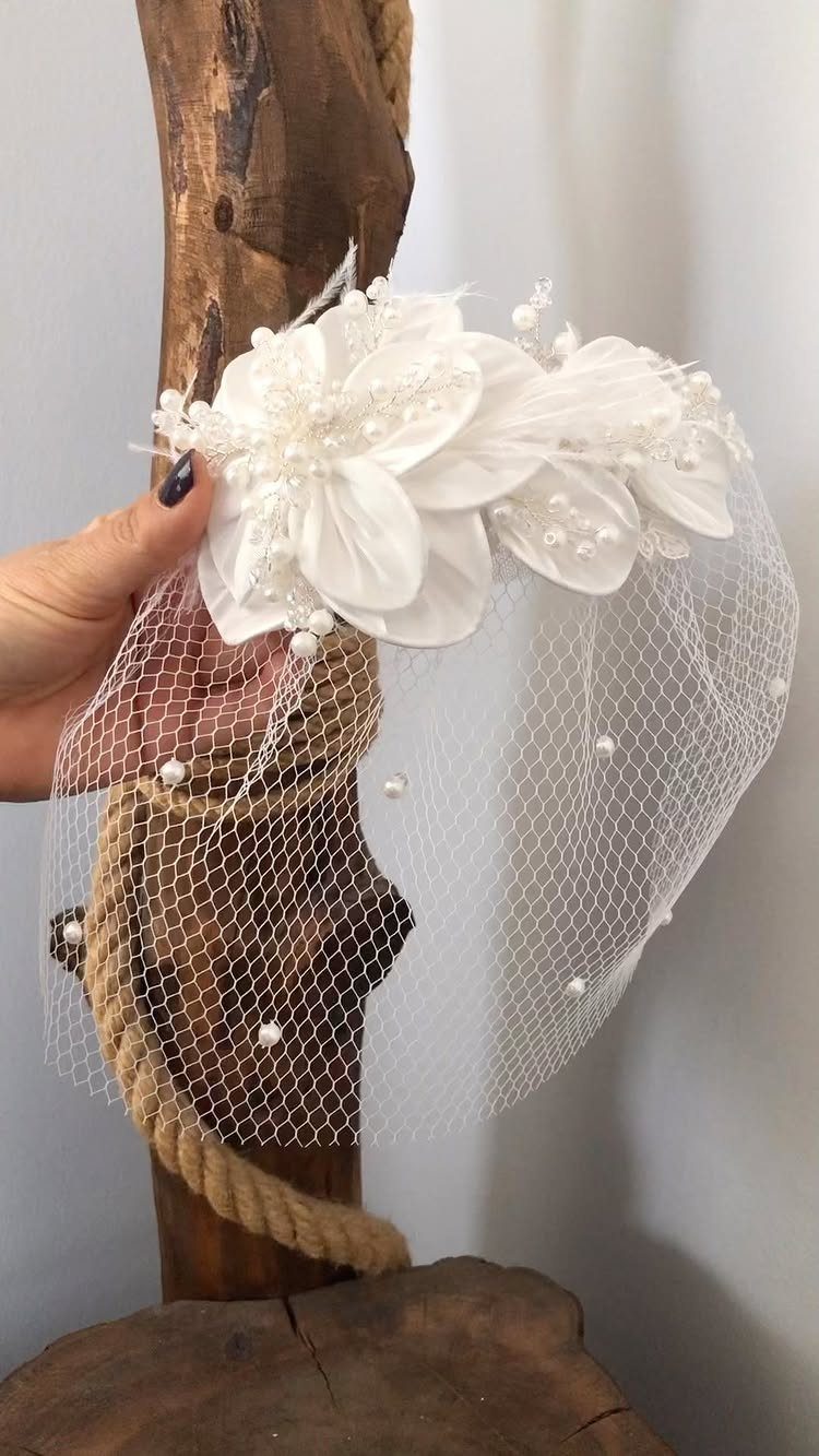 White bridal headpiece with a fabric flower and pearl-studded birdcage veil on wood.