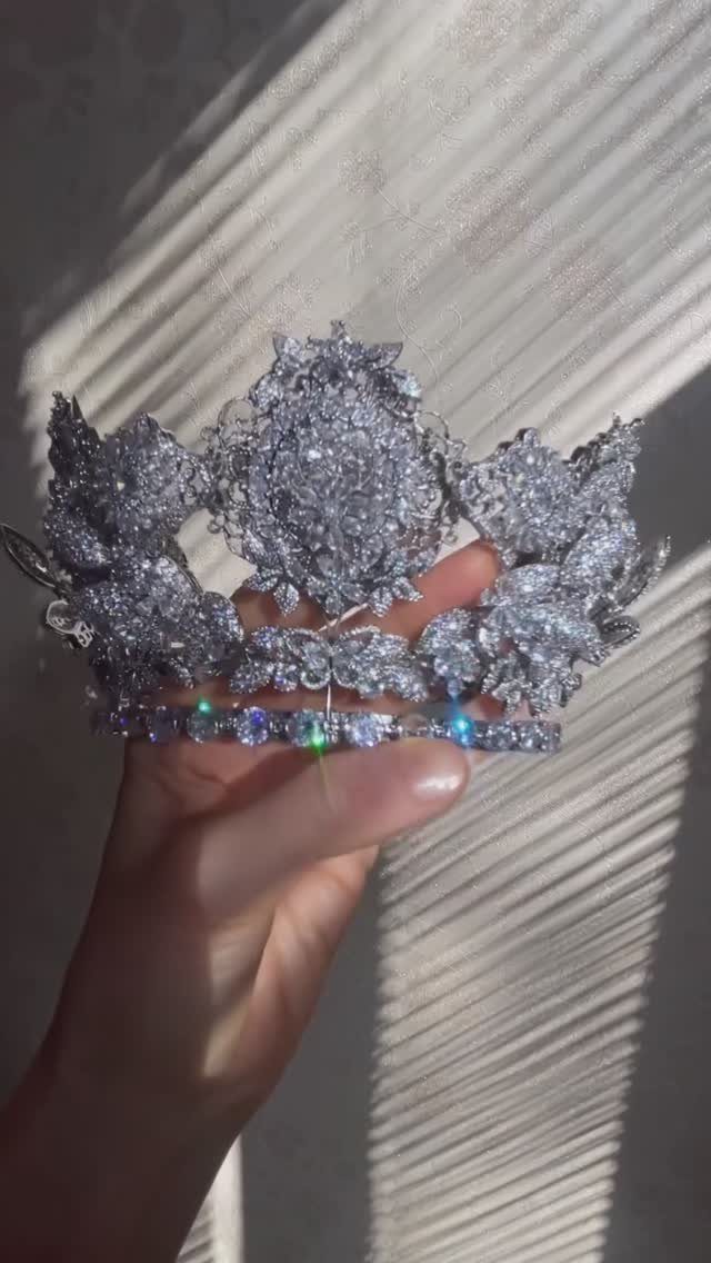 Silver bridal crown with sparkling crystals held up against white pleated fabric.