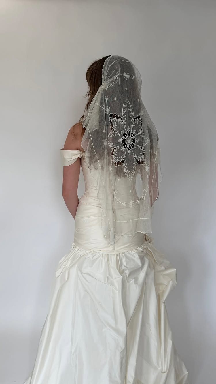 Woman in white bridal gown wearing a sheer veil with floral lace embroidery