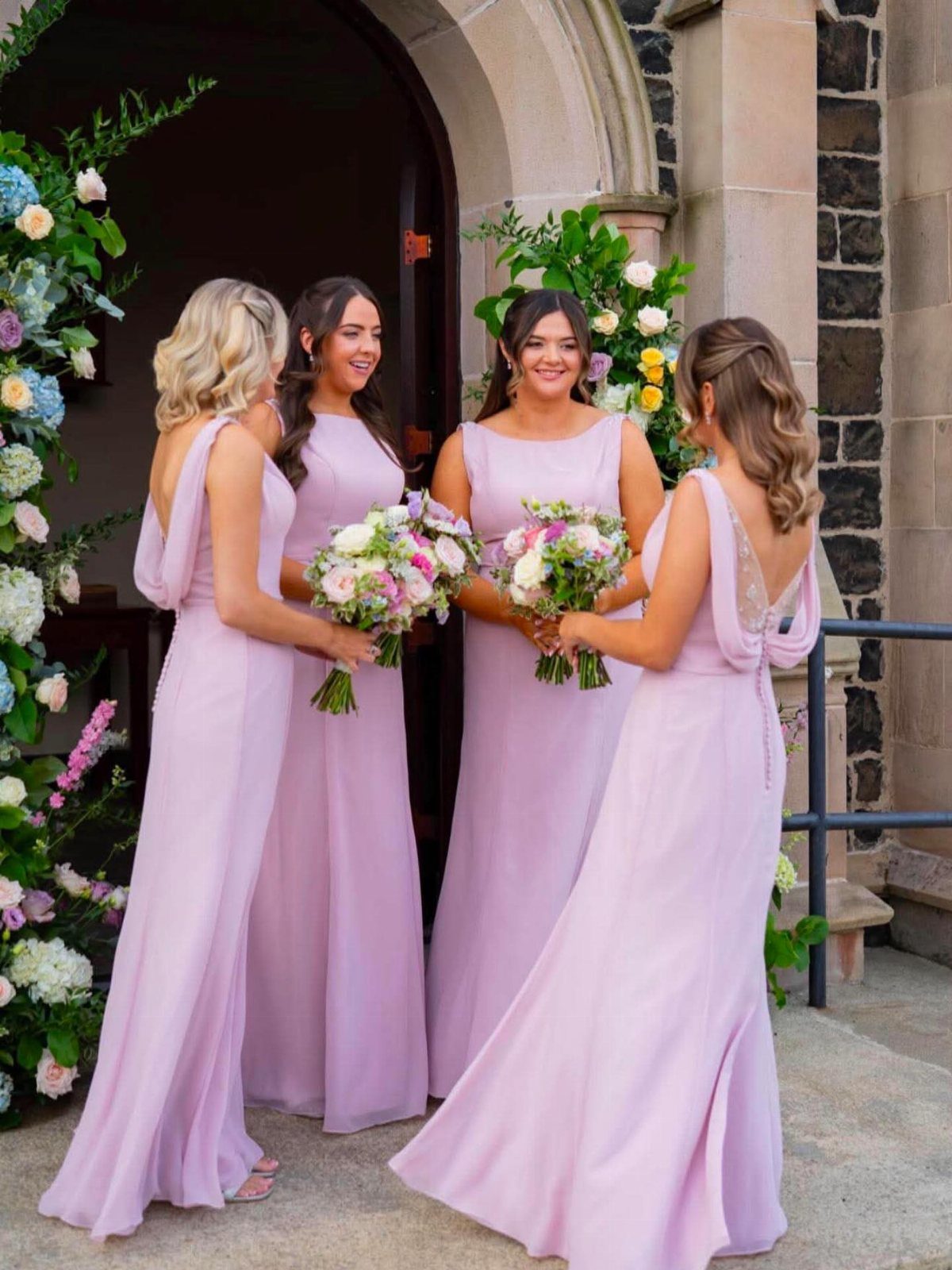 Four bridesmaids in different styles of light purple chiffon dresses holding bouquets.