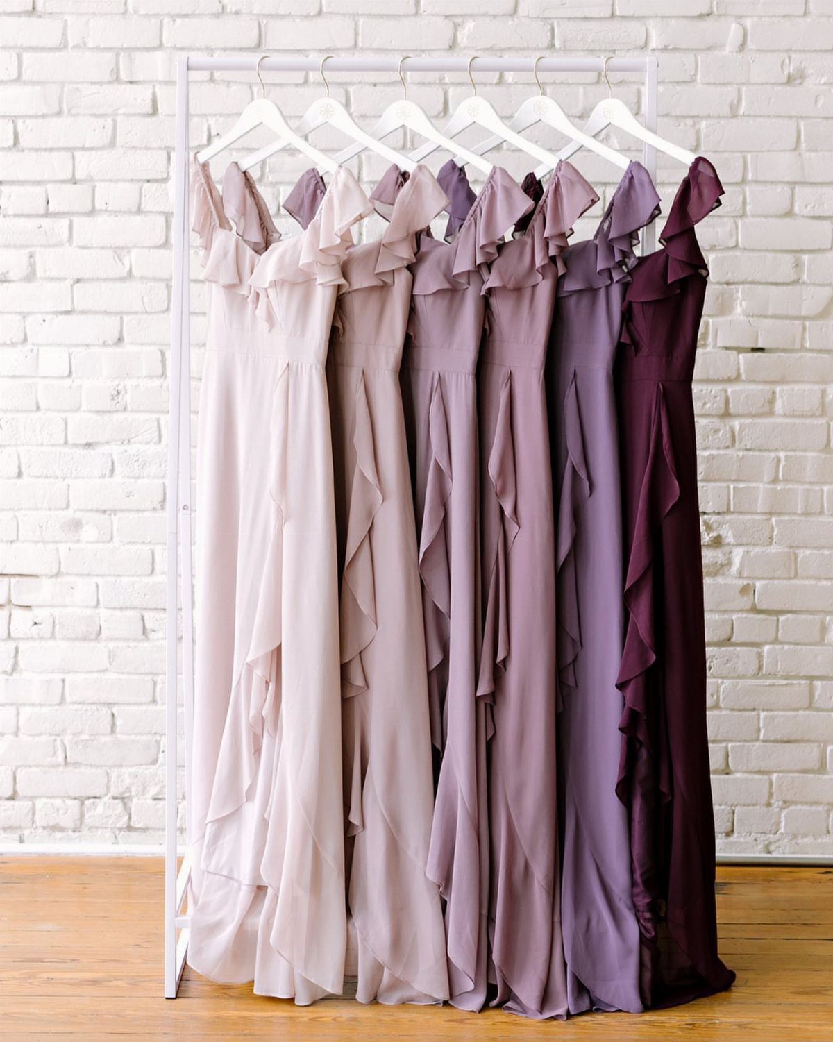Six purple dresses in ombre shades from light to dark on a rack.