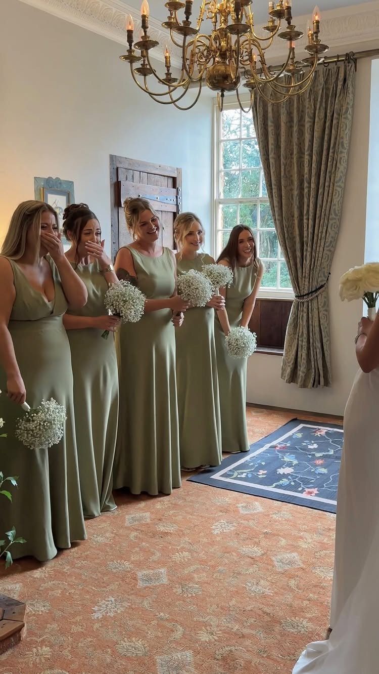 Five bridesmaids in olive green dresses of different styles holding white bouquets.