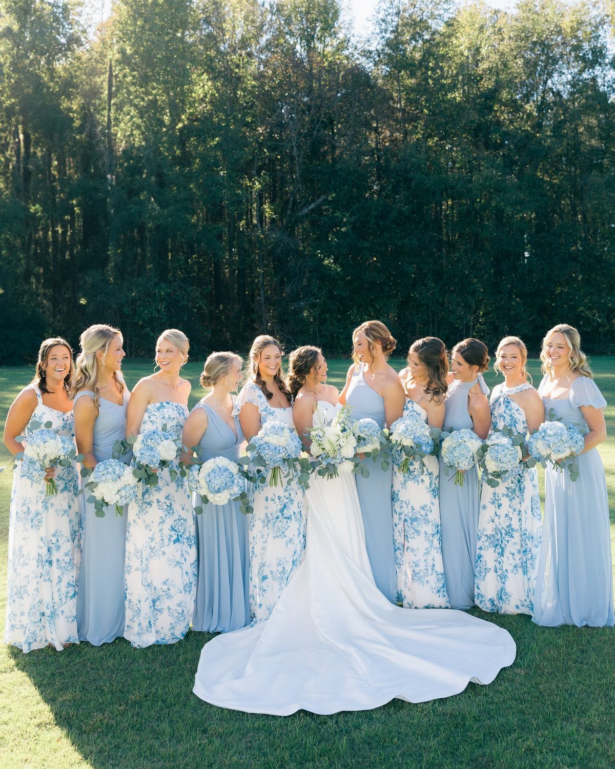 Bride and bridesmaids wearing a mix of solid and floral blue dresses outdoors.