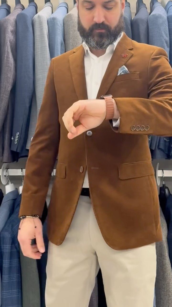 Man wearing a brown blazer and beige trousers checking his watch in a store