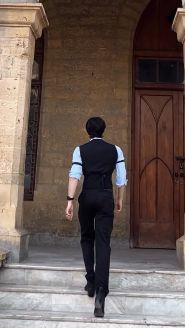 Man in light blue shirt and black waistcoat walking toward a wooden door