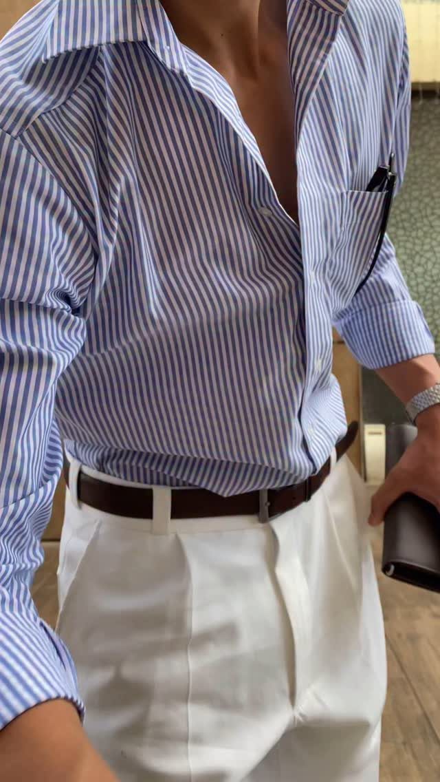Man wearing a blue striped shirt and white trousers with a brown belt.