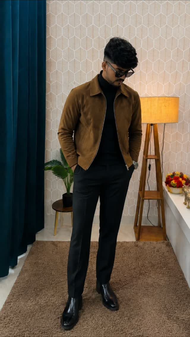 Man in brown suede jacket and black turtleneck posing in a modern room.