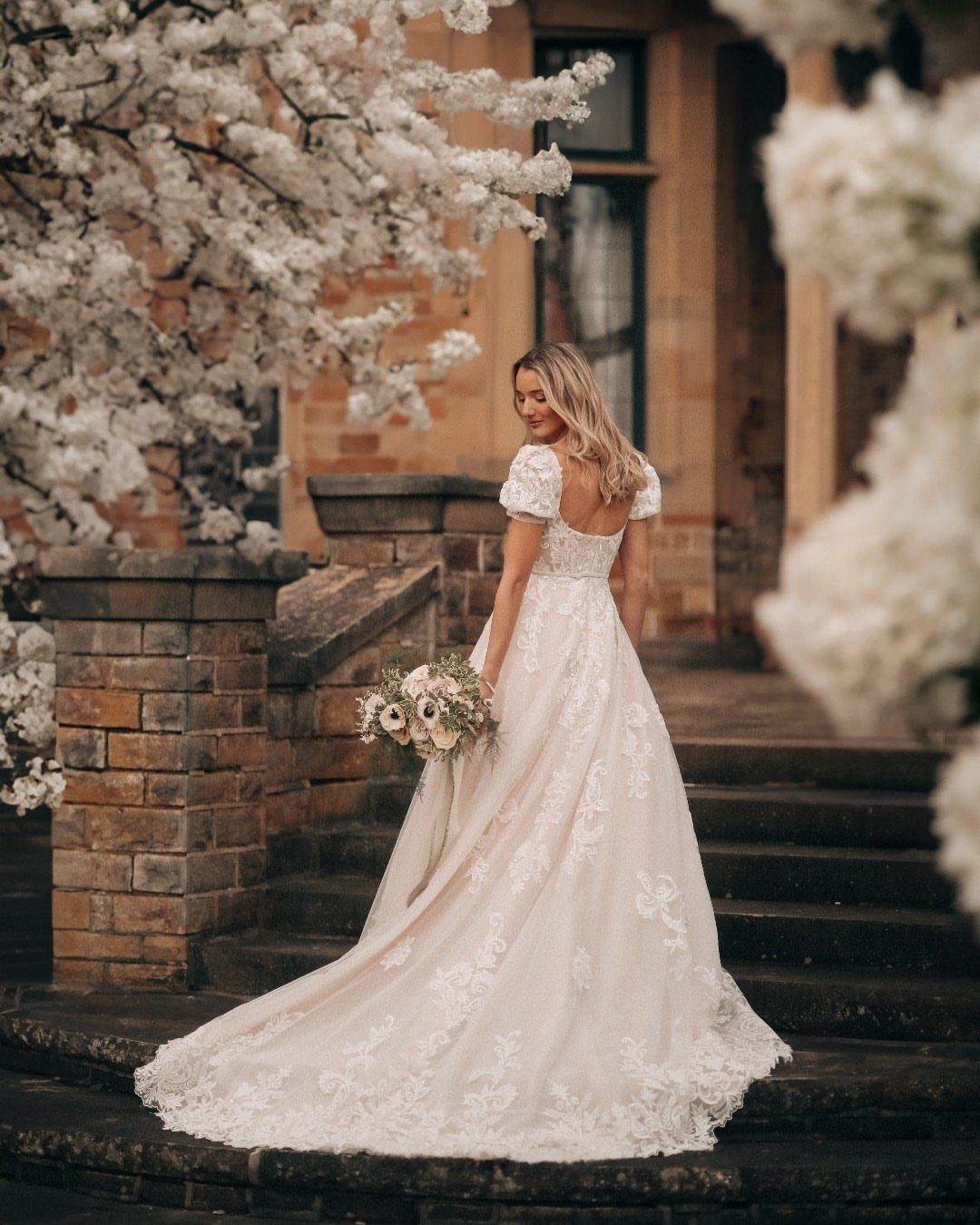 Bride in a white lace wedding dress with a long cathedral train on stone steps