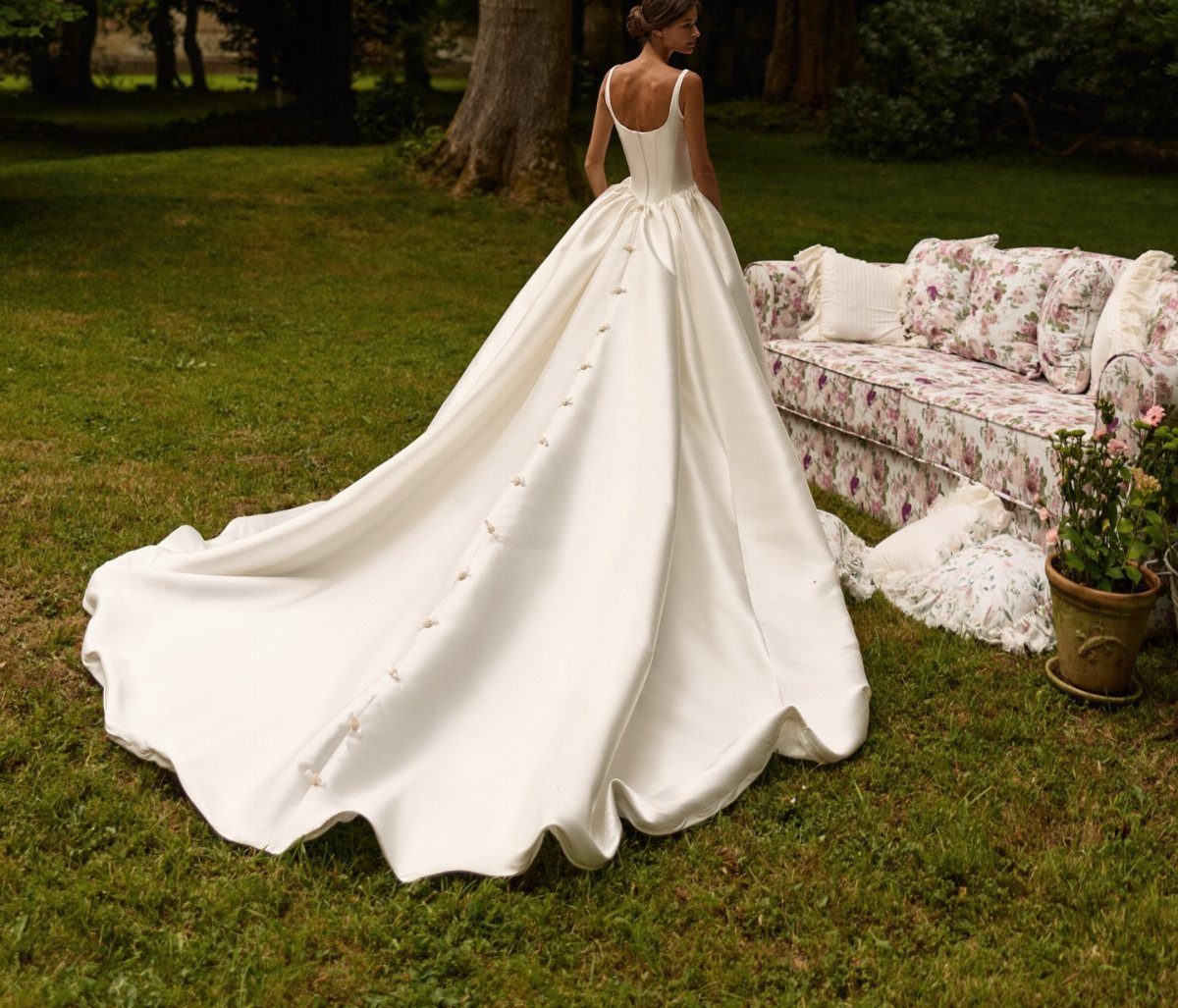 Woman in a white satin wedding dress with a long train on grass