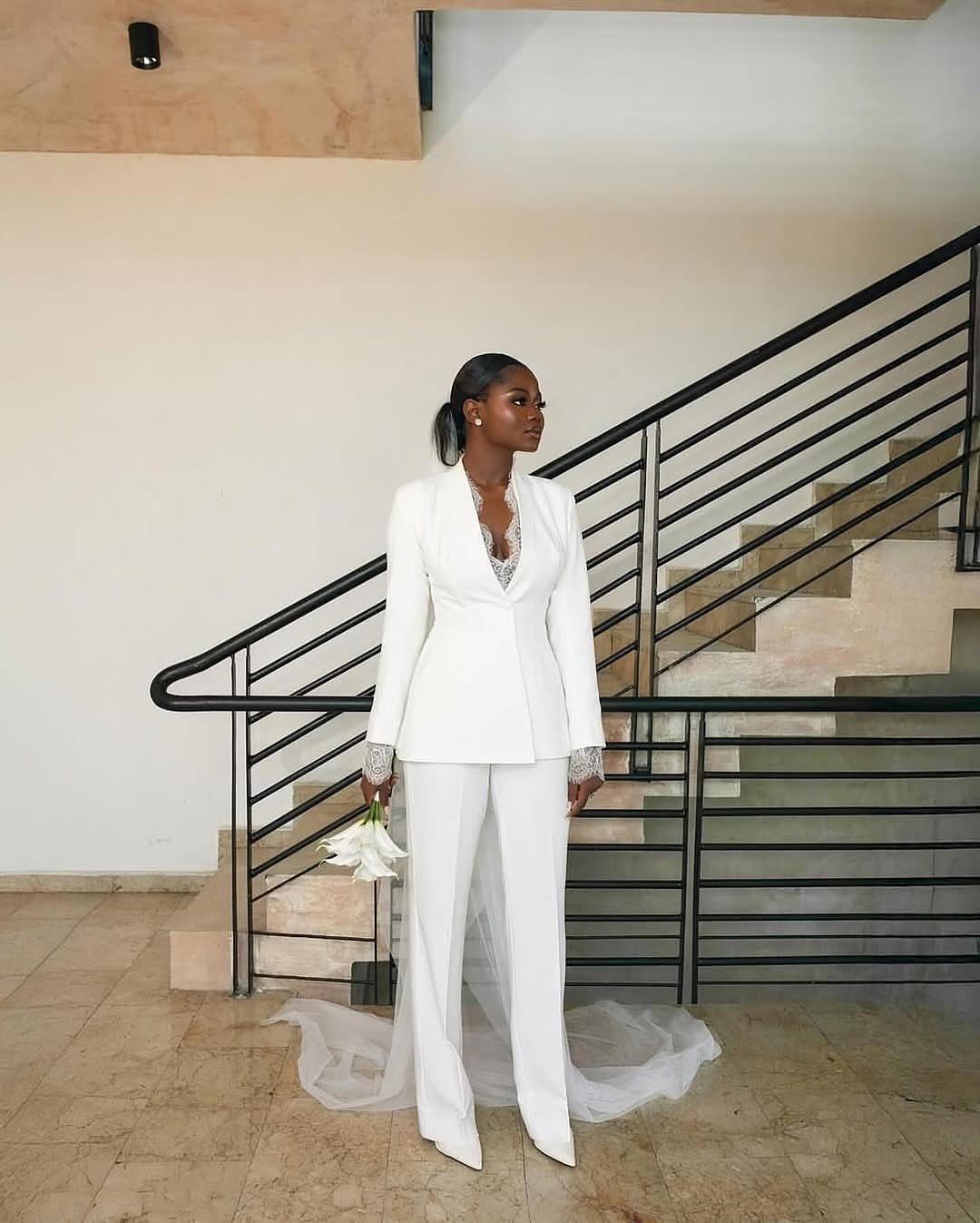 Woman in a chic white bridal pantsuit holding a white flower bouquet.
